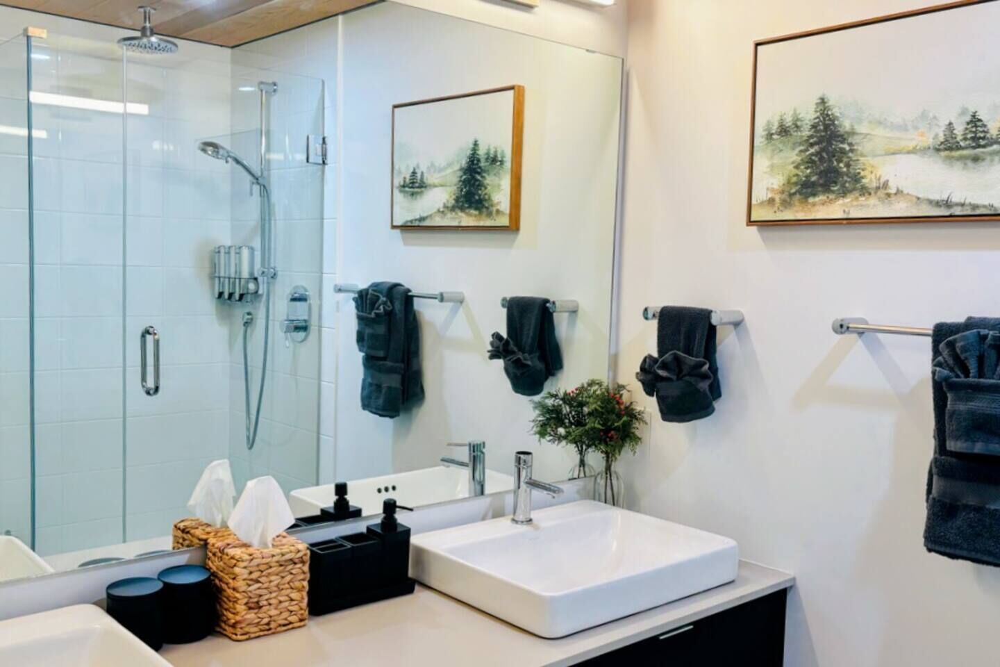 Uma casa de banho moderna com cabine de duche em vidro, uma sanita branca e duas pinturas emolduradas de paisagens na parede.