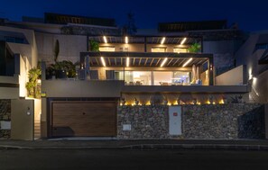 Ein modernes, zweistöckiges Haus mit Natursteinfassade, einer Garage und einem Balkon mit Außenbeleuchtung.
