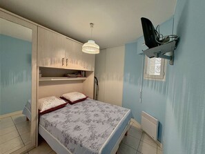 Ein Schlafzimmer mit Bett, Kleiderschrank, Deckenleuchte, Heizkörper und Fenster.