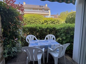 A patio with a table and chairs, surrounded by greenery and a building in the background. - Two-room apartment a stone's throw from the Port of Crouesty (ARZON)