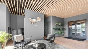 A modern lobby with a wooden slatted ceiling, a wall-mounted fish sculpture, a seating area with leather chairs, a round table, and a reception desk. - Two Hyve Homes, One Epic Nashville Stay (Nashville)