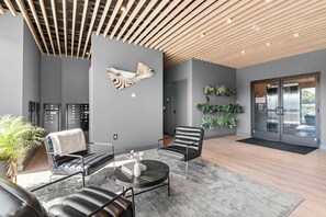 Eine moderne Lobby mit Holzbodenverkleidung, einer Wandskulptur in Fischform, einer Sitzecke mit Ledersesseln, einem runden Tisch und einer Rezeption.