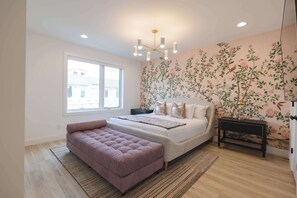 Ein Schlafzimmer mit einem großen Bett, einer Bank, einem Nachttisch, einer Wand mit Blumenmuster und einem Fenster.