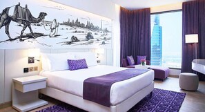 Ein modernes Hotelzimmer mit einem großen Bett, einem Wandgemälde mit Stadtansicht, Blick auf ein Hochhaus und einer Sitzgelegenheit in Lila.