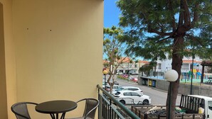 Ein Balkon mit Tisch und Stühlen, Blick auf eine Straße mit Autos und ein Spielplatz im Hintergrund.