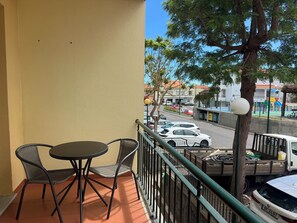 Ein Balkon mit Tisch und Stühlen, Blick auf eine Straße mit Autos und ein Spielplatz im Hintergrund.