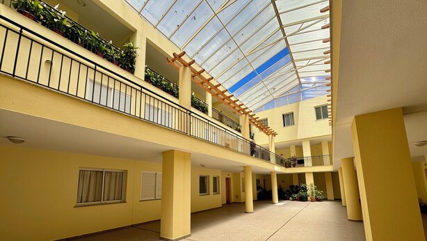 Ein mehrgeschossiges Atrium mit Glasdecke, gelben Wänden und Kübelpflanzen.