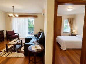 Ein Zimmer mit einem Bett, einem Schlafsofa, einem Sessel, einem kleinen Tisch und einem Fenster mit Vorhängen.