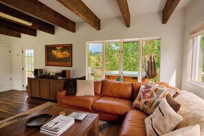 A living room with a leather sofa, wooden beams, a large window, and a painting on the wall.