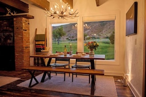 A dining area with a brick fireplace, wooden table, benches, and a chandelier.