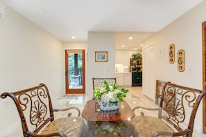 A dining area with a glass table, metal chairs, a vase with flowers, and a kitchen in the background.