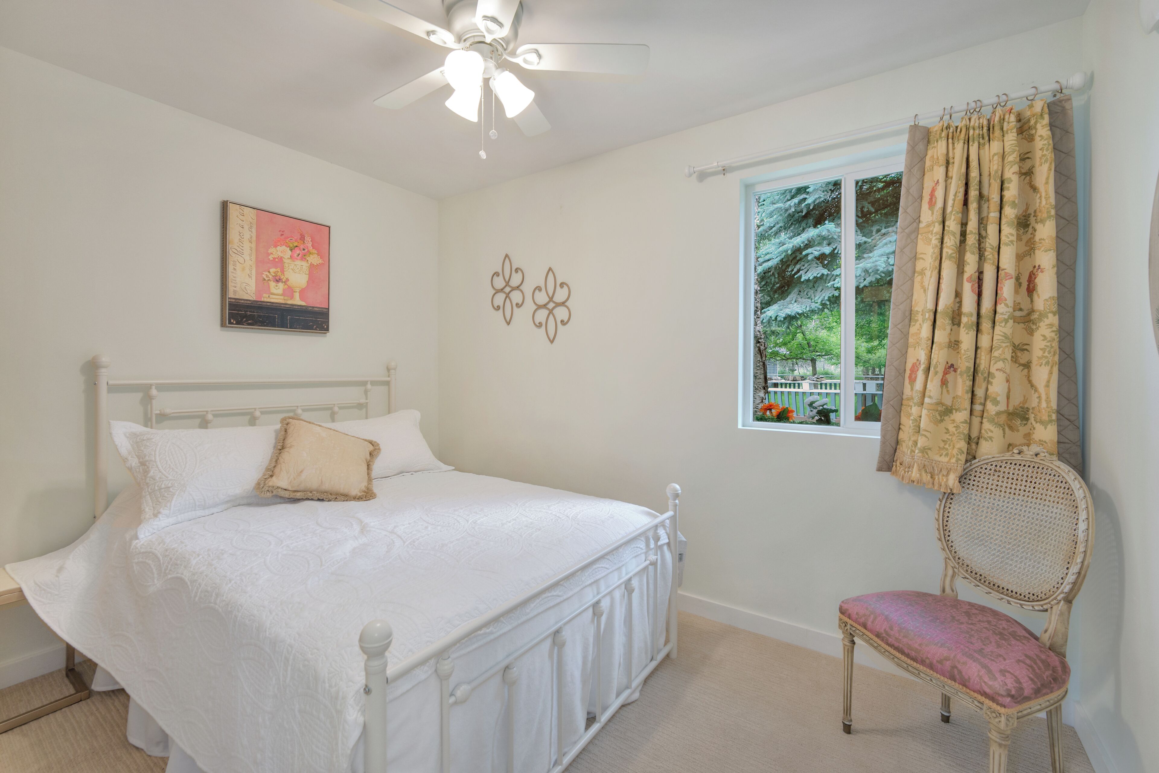A bedroom with a bed, a chair, a ceiling fan, a window with curtains, and wall decor.