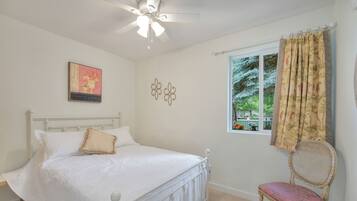A bedroom with a bed, a chair, a ceiling fan, a window with curtains, and wall decor.