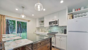 A modern kitchen with white cabinets, a microwave, a refrigerator, and a large island with a glass top.