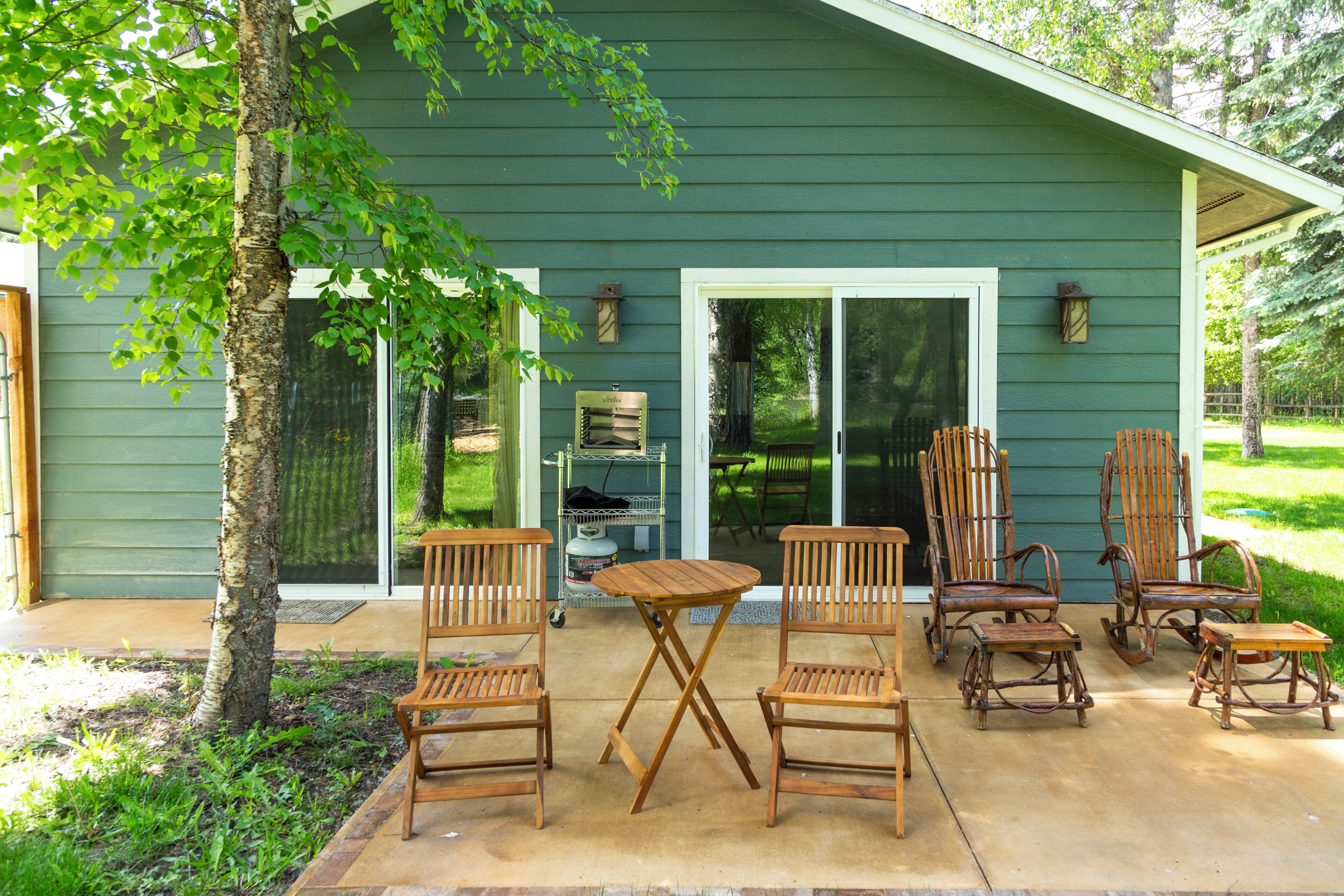 A green house with a patio, wooden chairs, a table, and a grill.
