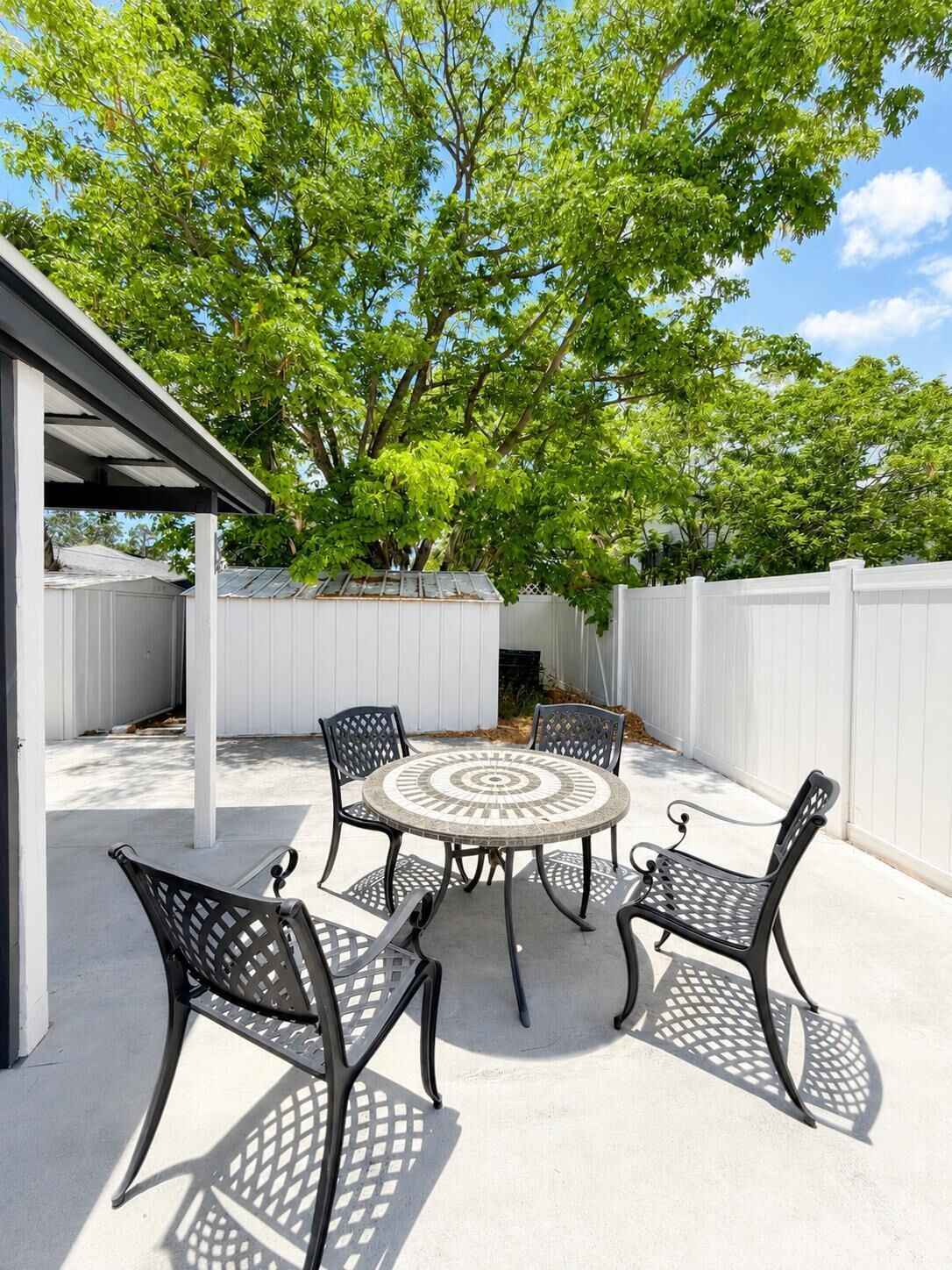 Une terrasse avec une table ronde et quatre chaises, entourée d’une clôture blanche et d’arbres.