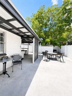 Ein überdachter Patio-Bereich mit Gartenmöbeln, einem Tisch und Stühlen.