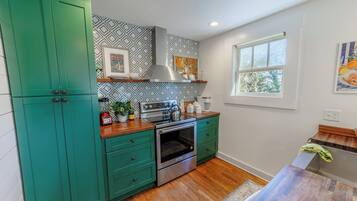 Una cocina con armarios color turquesa, un horno de acero inoxidable y un ventanal con vista a árboles.