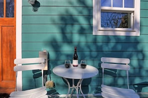 Ett hus med en fasad i en nyans av turkos, en vit dörr, ett fönster och ett litet runt bord med två stolar.