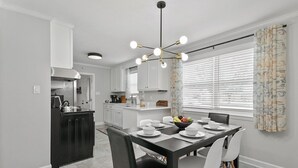 Une cuisine moderne avec des meubles blancs, un îlot central noir et un coin repas comprenant une table noire et des chaises blanches.