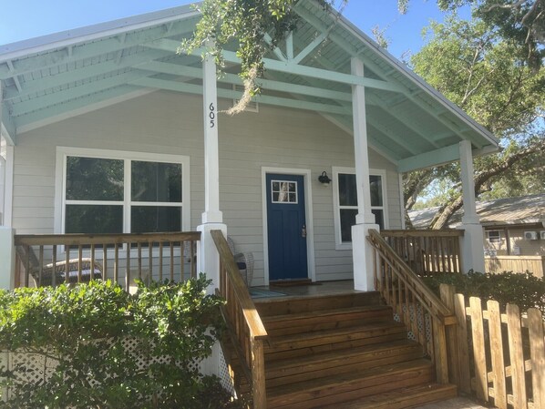 Een huis met een veranda, een blauwe deur en het nummer 605 op de paal.