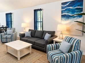 Ein Wohnzimmer mit einer Couch, zwei gestreifte Sesseln, einem Couchtisch und einem Gemälde von Wellen.