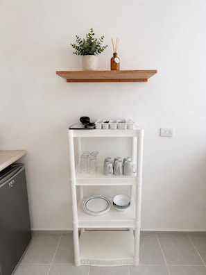 Un estante blanco con utensilios de cocina y una planta en maceta encima.