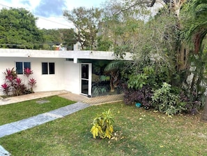 A modern house with a white exterior, a small front yard, and a variety of plants and trees. - Casa Balam Cayo Lobo (Cancún)