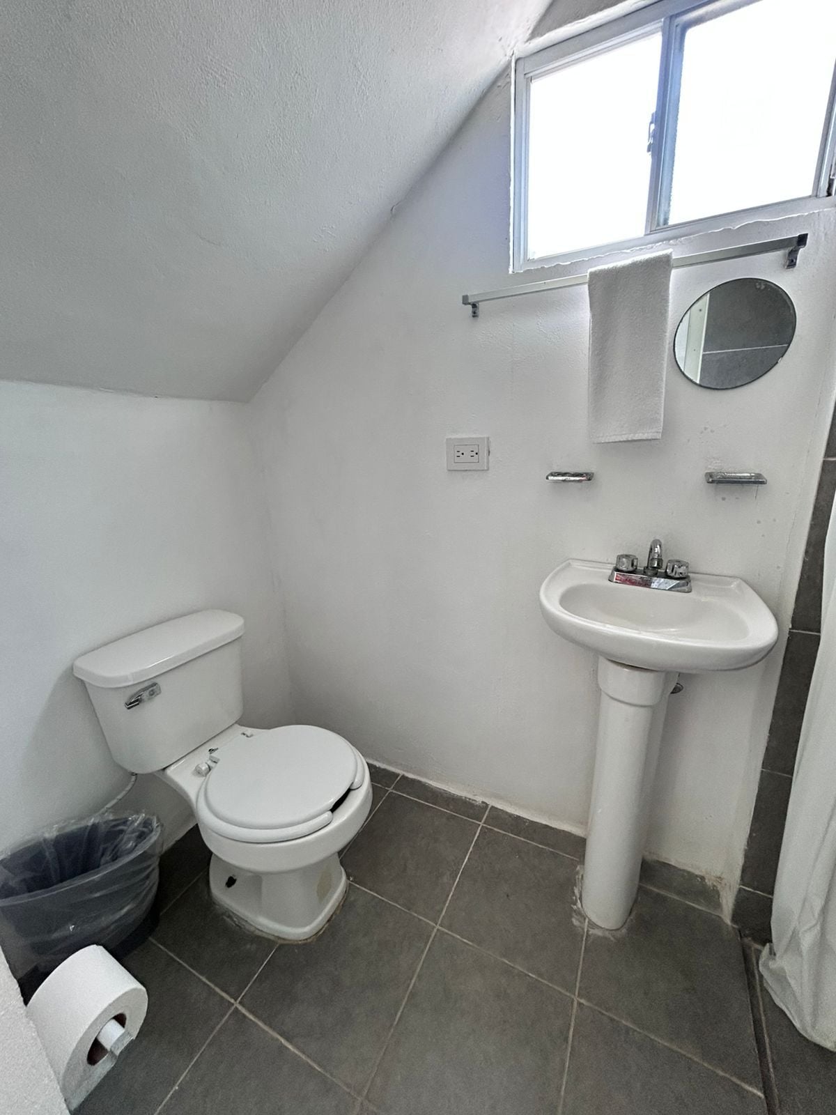 A small, white bathroom with a toilet, sink, and a window.