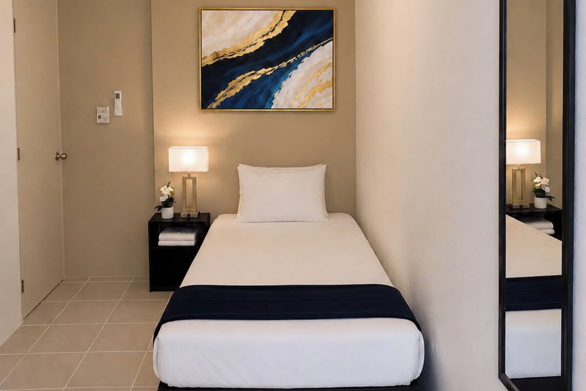 Una habitación de hotel con cama, mesitas de noche, ventilador de techo, espejo en la pared y un cuadro.