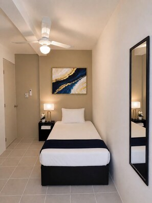 A hotel room with a bed, nightstands, a ceiling fan, a wall-mounted mirror, and a painting.