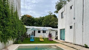 A swimming pool with a small deck area, a white building with a flat roof, and a green lawn with outdoor furniture. - Casa Balam Cayo Lobo (Cancún)
