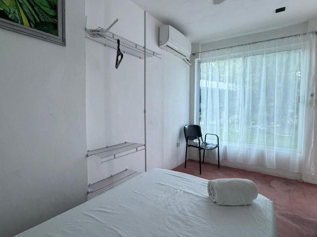 A hotel room with a bed, a chair, a radiator, and a window with sheer curtains.