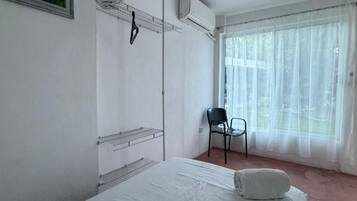 A hotel room with a bed, a chair, a radiator, and a window with sheer curtains.