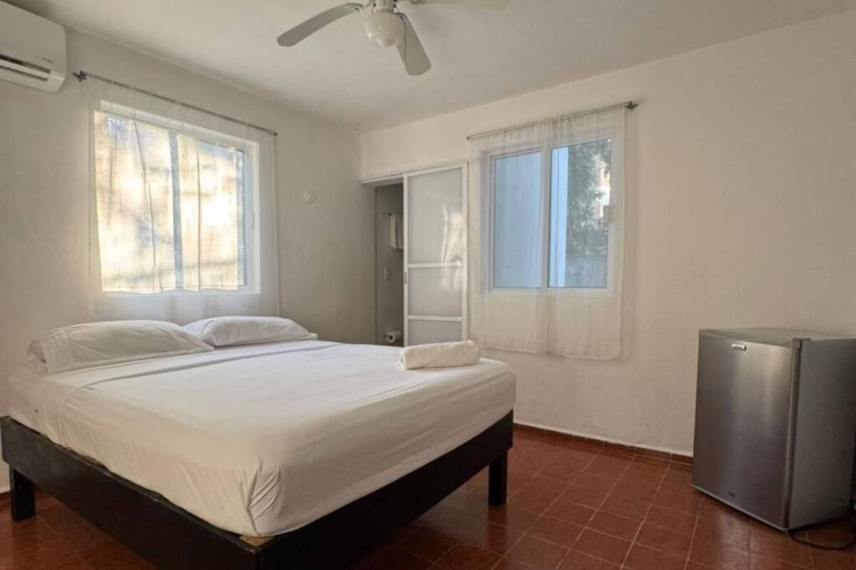 Une chambre à coucher avec un lit, un ventilateur de plafond, une fenêtre et un réfrigérateur.