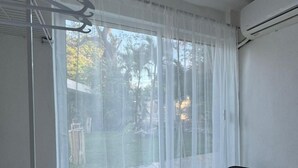 A room with a large window covered by sheer curtains, a black chair, and an air conditioning unit on the wall. - Casa Balam Cayo Lobo (Cancún)