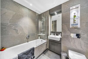 A modern bathroom with a glass-enclosed shower, a white bathtub, a vanity with a mirror, and a toilet. - Spacious Woolwich Apartment with sea view (London)