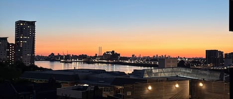 A cityscape at dusk with a river, buildings, and a bridge.