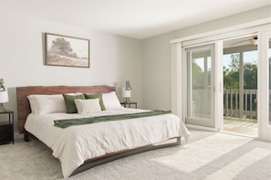 A bedroom with a bed, two nightstands, a lamp, a framed picture, and a sliding glass door to a balcony.