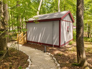 Eine kleine Holzhütte mit roter Umrandung, umgeben von Bäumen und einem Kiesweg.