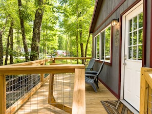 Eine Holzdielen-Terrasse mit Metallgeländer, eine Tür mit Fußmatte und ein Stuhl.