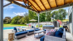 A covered patio with wicker furniture, a hot tub, and a barbecue grill. - Spacious Country Retreat | Pool • Hot Tub • Sauna • 5 King Bedrooms (Walla Walla)