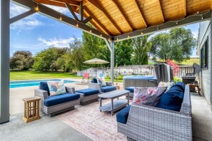 Une terrasse couverte avec des meubles en osier, un jacuzzi et un barbecue.