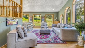 A spacious living room with a staircase, large windows, and a colorful rug. - Spacious Country Retreat | Pool • Hot Tub • Sauna • 5 King Bedrooms (Walla Walla)