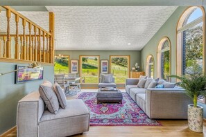 Un salon spacieux avec un escalier, de grandes fenêtres et un tapis aux couleurs vives.