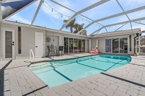 A covered outdoor swimming pool with a patio area, seating, and a flamingo decoration. - Gulf Access Retreat with Heated Saltwater Pool, Dock & Sunset Views - Golden Sunset Villa - Roelens (Cape Coral)