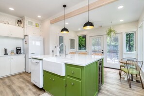 A modern kitchen with white cabinets, a green island, a white refrigerator, and pendant lighting. - The Reserve Extended Stay (Walla Walla)