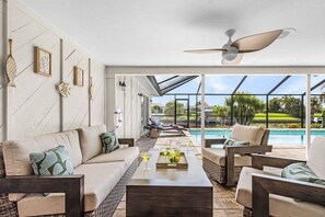 Ein moderner Innenpoolbereich mit einer Couch, Sesseln und einem Deckenventilator.