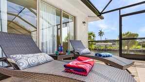 Uma sala de sol com poltronas de vime, uma janela grande e vista para palmeiras.