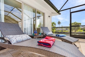A sunroom with wicker lounge chairs, a large window, and a view of palm trees. - Waterfront Fun with Gulf Access, Heated Saltwater Pool & Dock - Channelside Paradise - Roelens (Cape Coral)